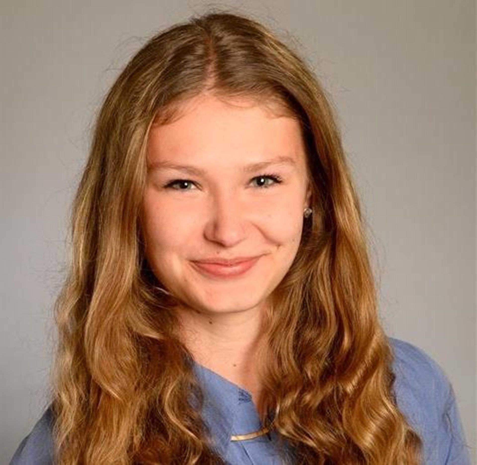 Zu sehen ist eine junge Frau mit langen lockigen, dunkelblonden Haaren, die in die Kamera lächelt. Hierbei handelt es sich um ein Portrait. 